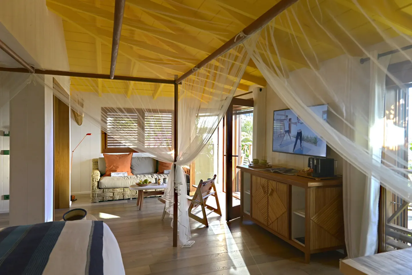 Guest room with netted bed, sofa, and wood ceiling at Hotel Manapany.