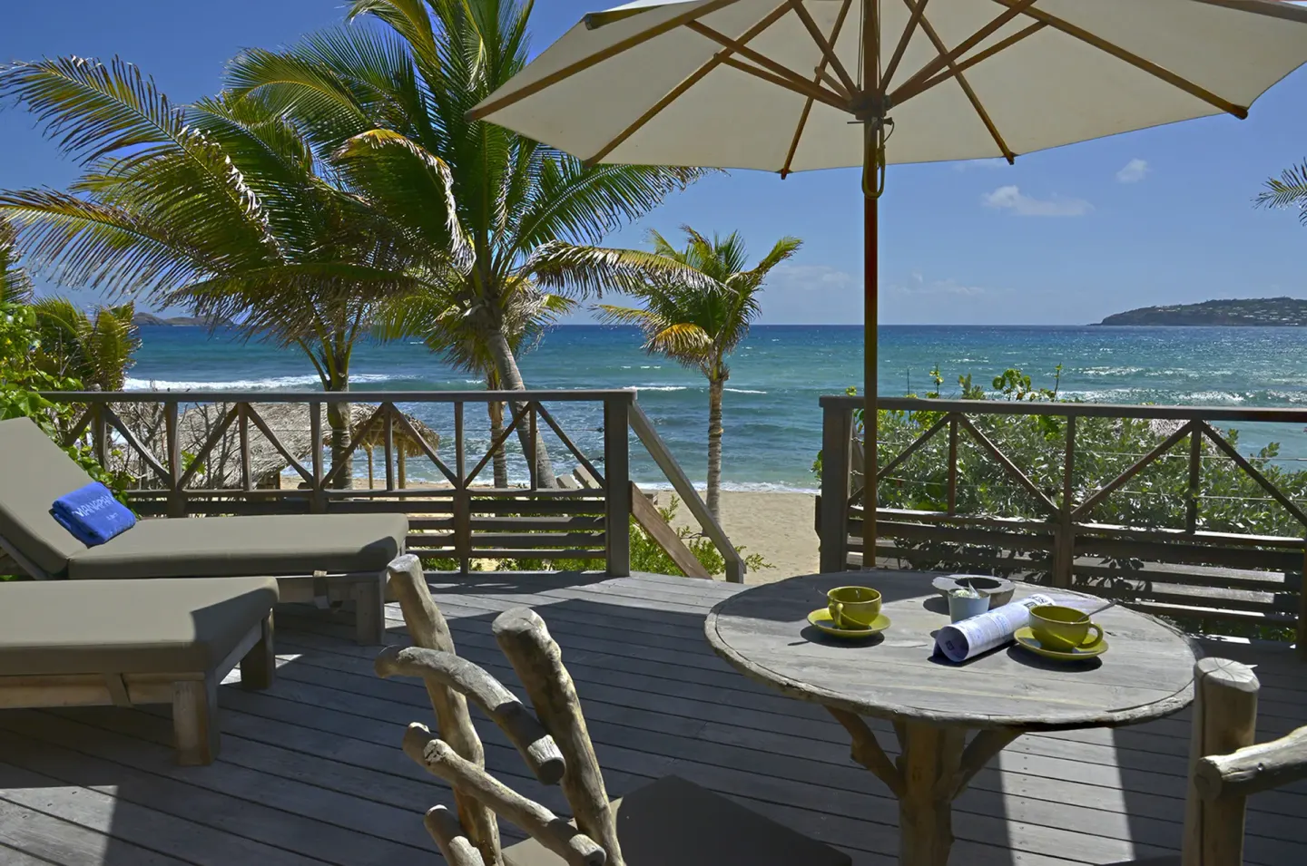 Oceanfront deck with loungers, umbrella, and coffee cups at Hotel Manapany.