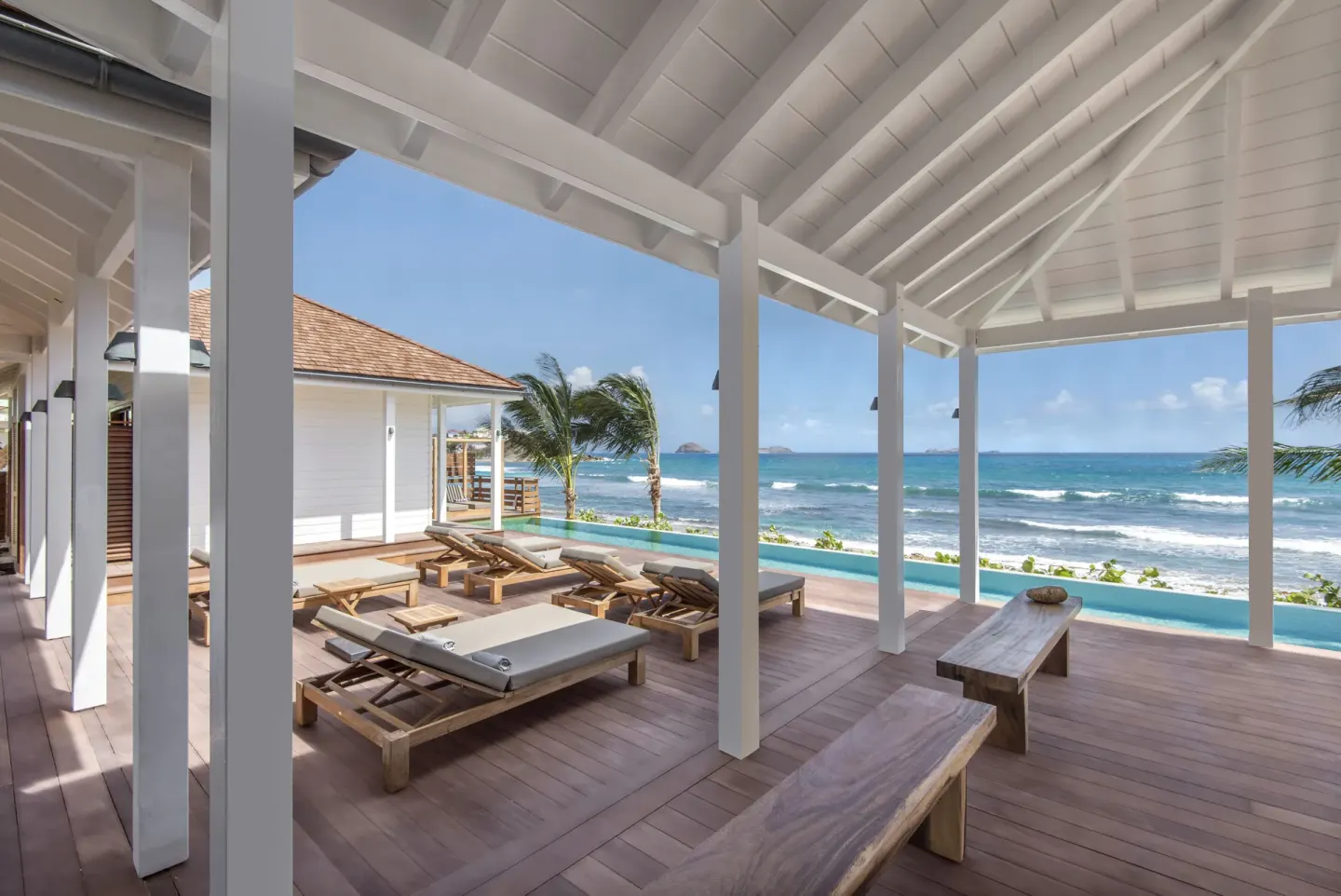 Covered oceanfront deck with loungers, benches and pool at Hotel Manapany.