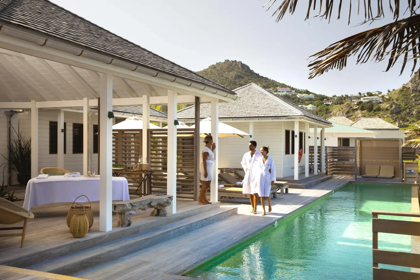 Guests in robes beside a pool and spa treatment table at Hotel Manapany.