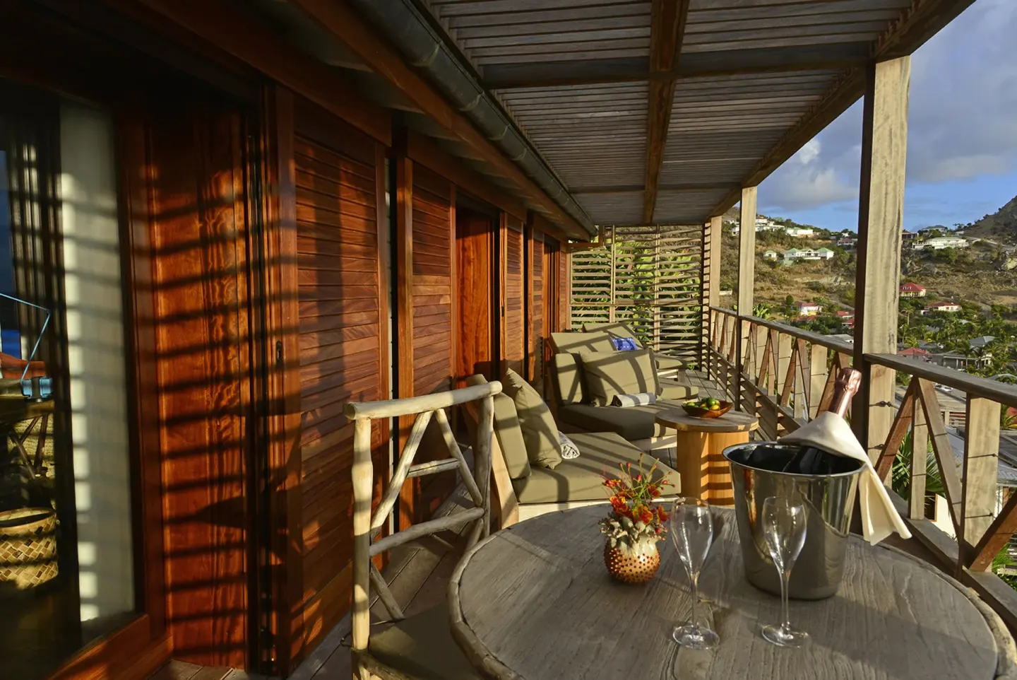 Private wooden balcony with loungers and a table set with glasses at Hotel Manapany.