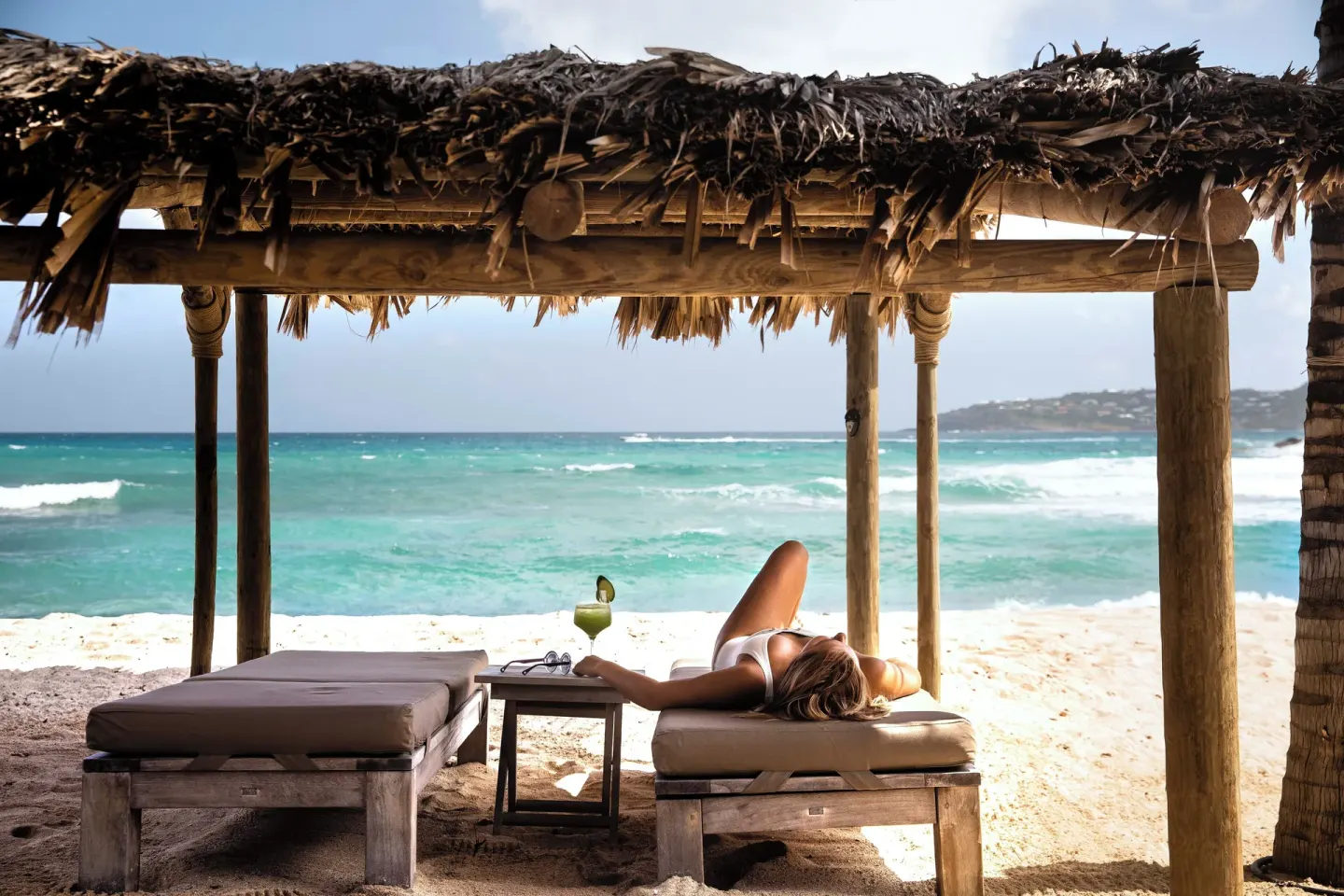 Guest relaxing on a beach lounger under a thatched shelter at Hotel Manapany.