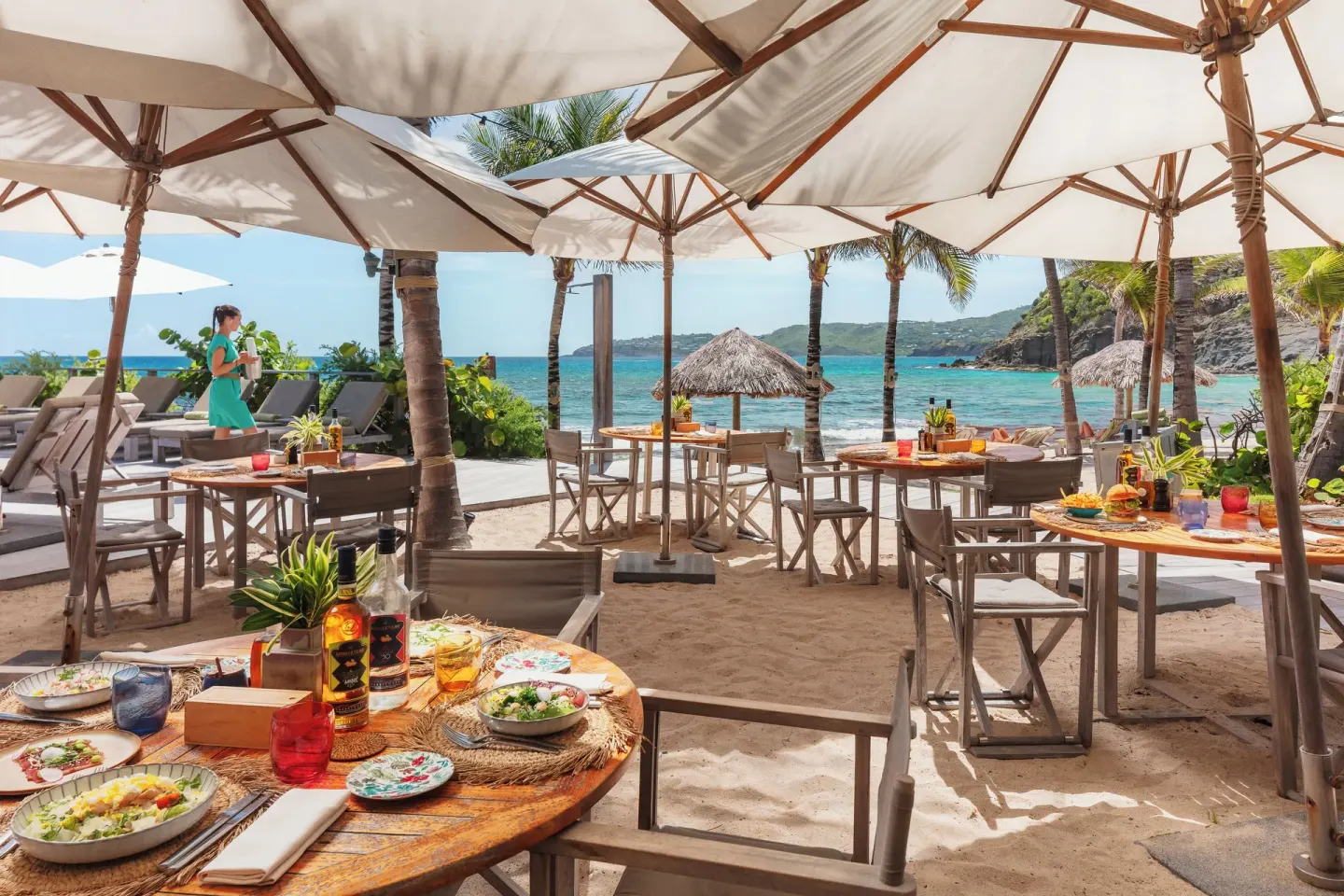 Beachfront dining tables on sand beneath umbrellas at Hotel Manapany.