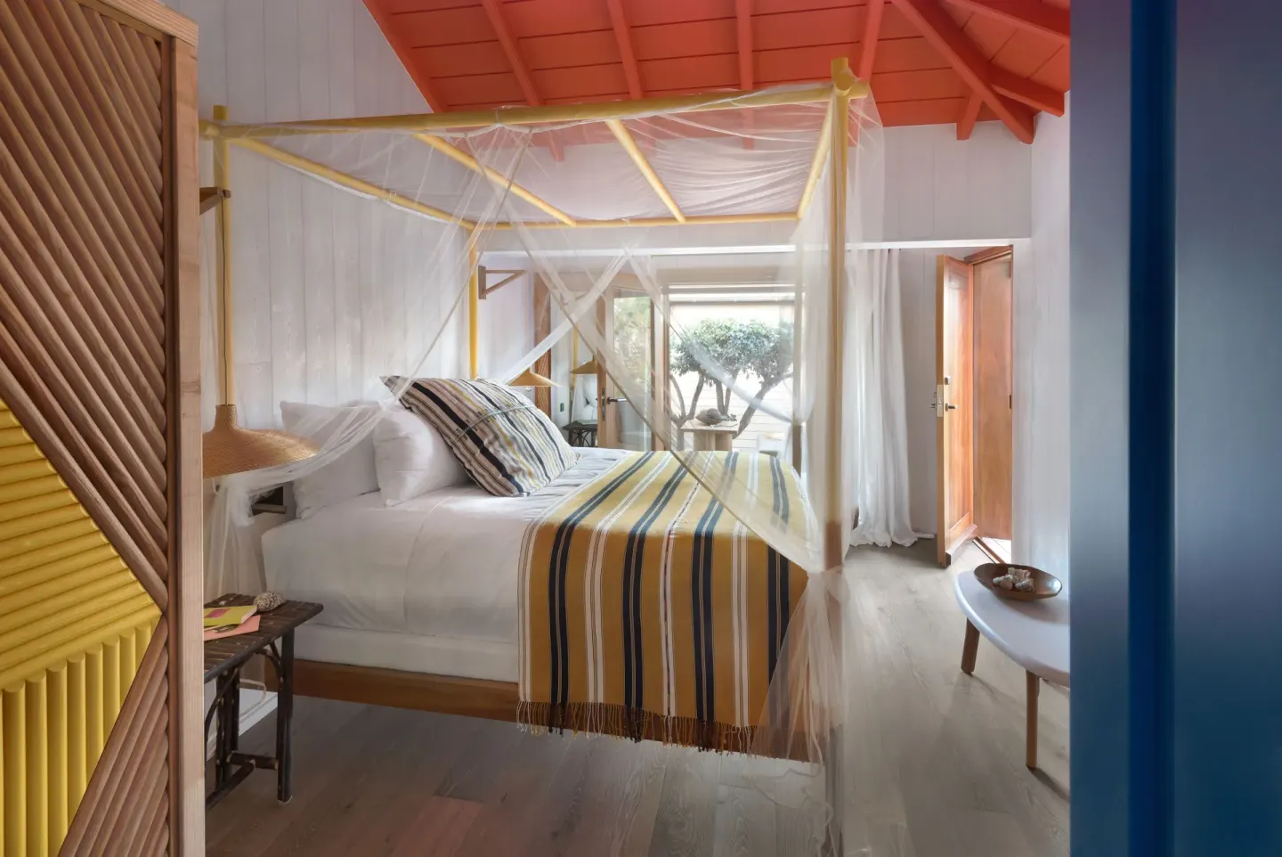 Garden View Room with yellow canopy bed and open doorway at Hotel Manapany.