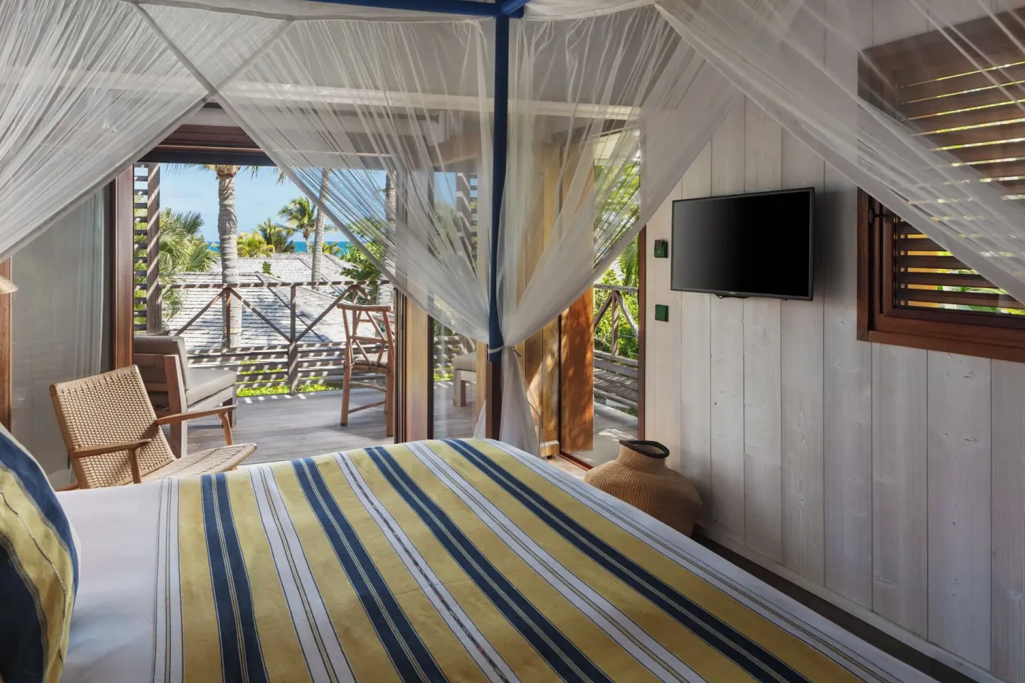 Garden View Room bed with mosquito net, TV, balcony, palms, and sea glimpse at Hotel Manapany.