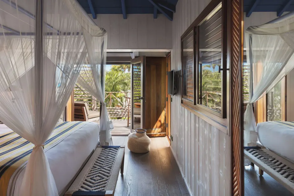 Garden View Room with netted bed, bench, mirror, and balcony door at Hotel Manapany.