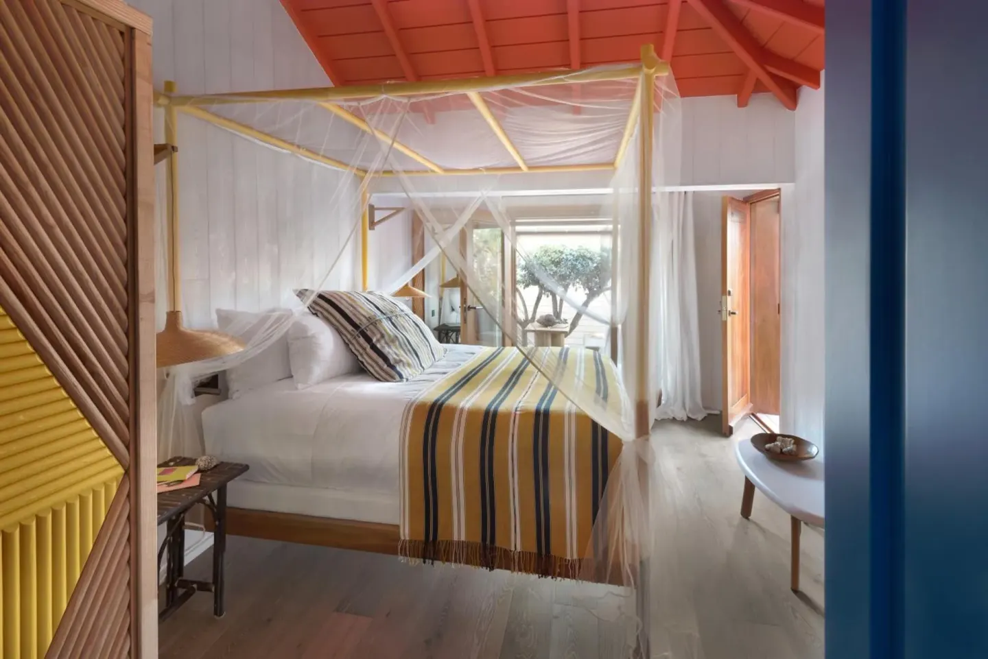 Tropical Room bed with mosquito net and striped throw at Hotel Manapany.