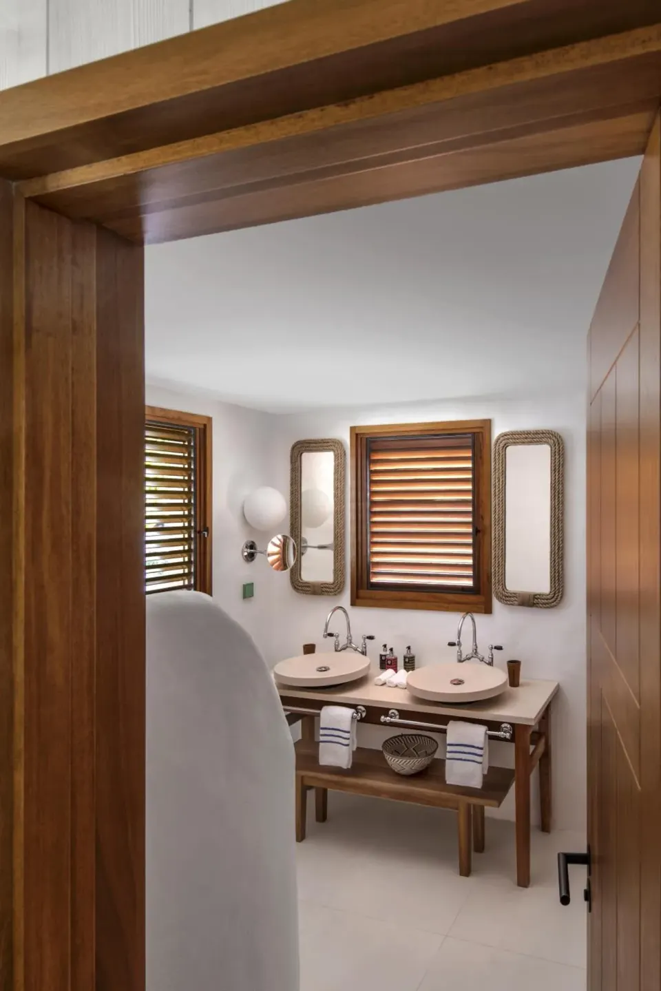 Tropical Room bathroom with twin sinks and shuttered windows at Hotel Manapany.