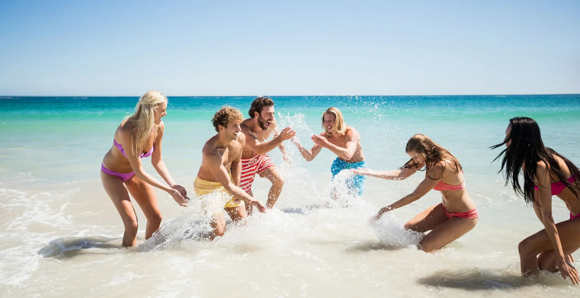 Group splashing in shallow turquoise water on the beach at Hotel Mousai Cancun.