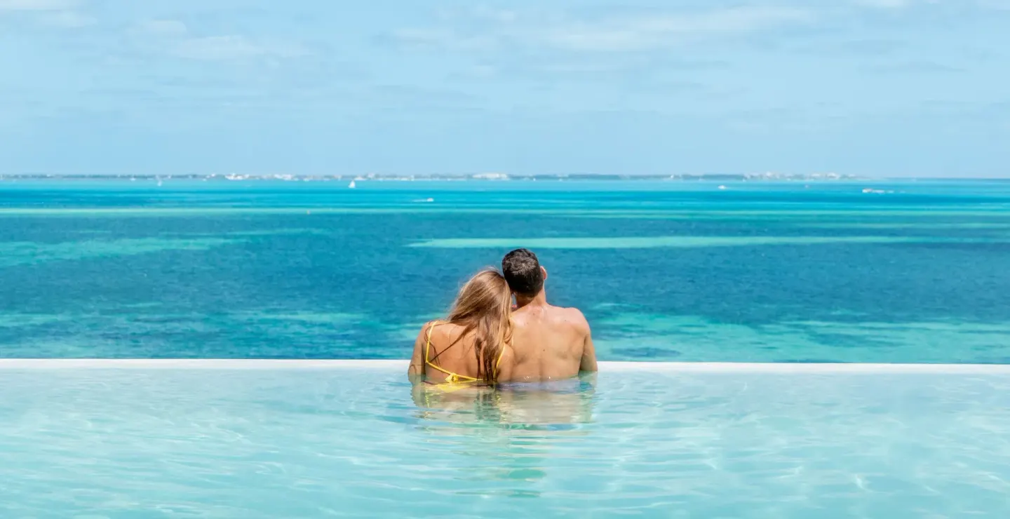 Couple in an infinity pool overlooking turquoise water at Hotel Mousai Cancun.