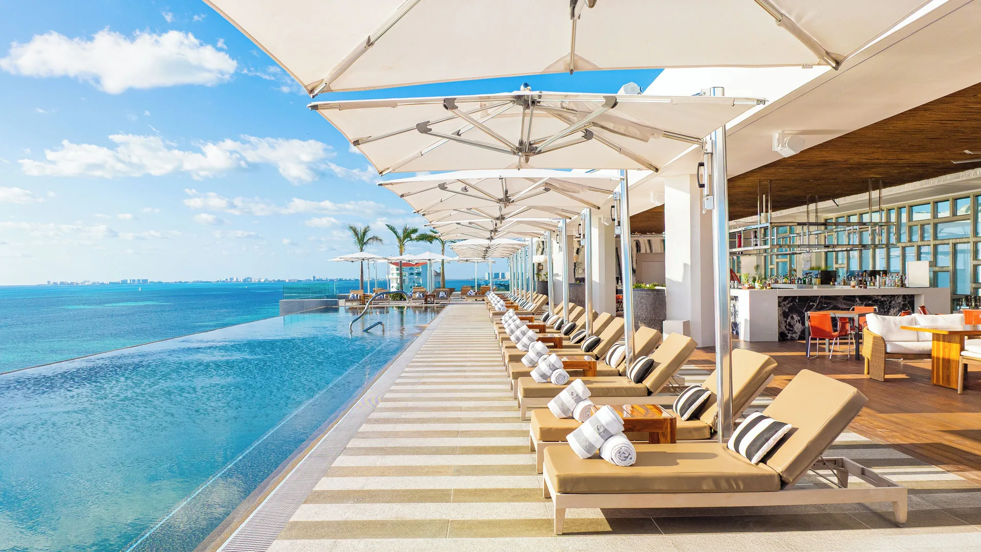 Infinity pool deck with loungers and umbrellas at Hotel Mousai Cancun.