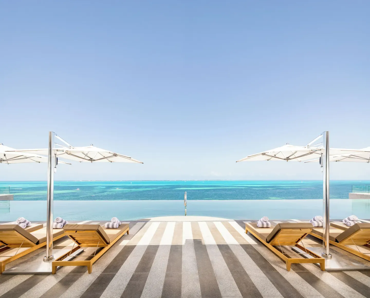 Symmetrical infinity pool deck with loungers and ocean view at Hotel Mousai Cancun.