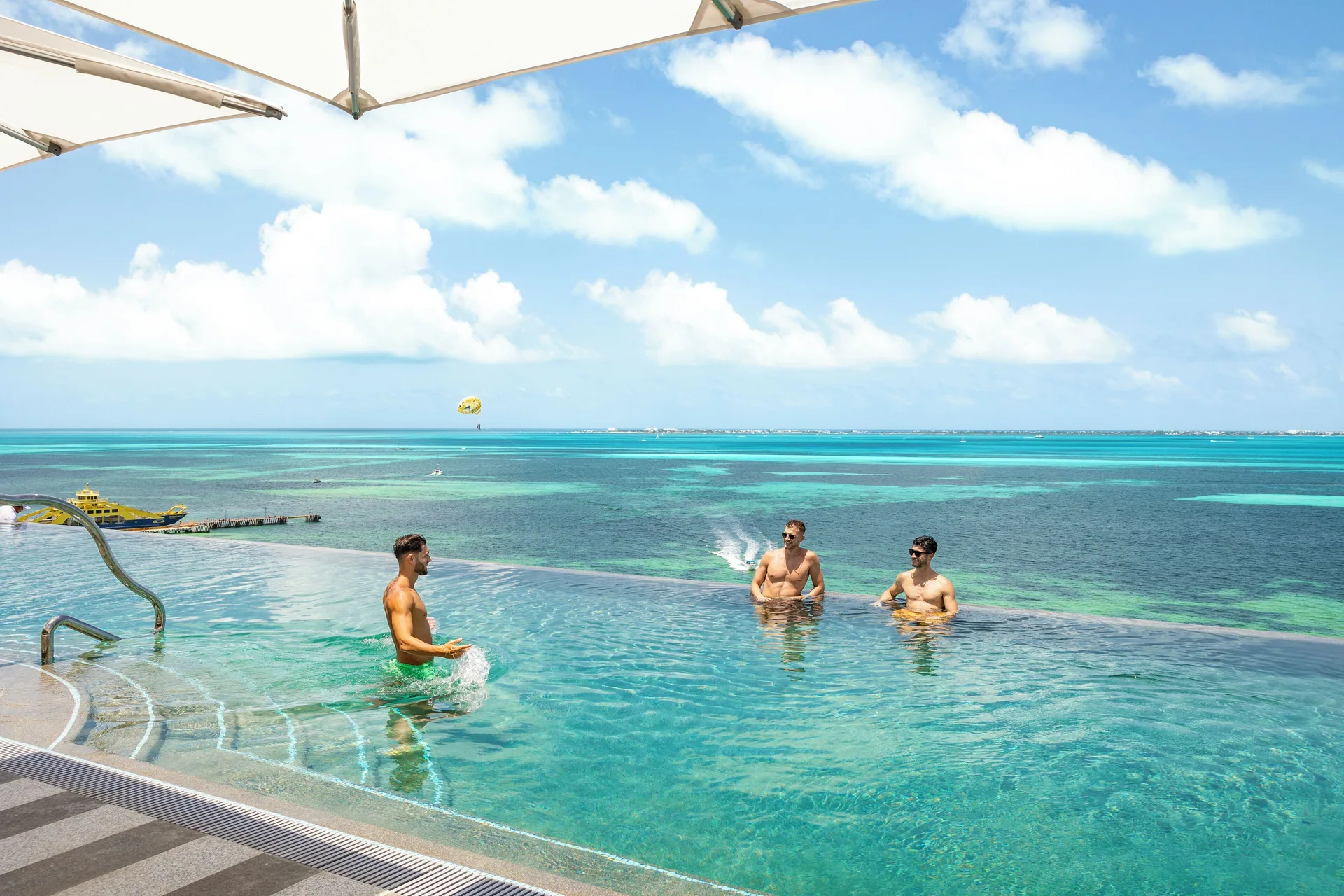 Guests playing in an infinity pool overlooking turquoise water at Hotel Mousai Cancun.
