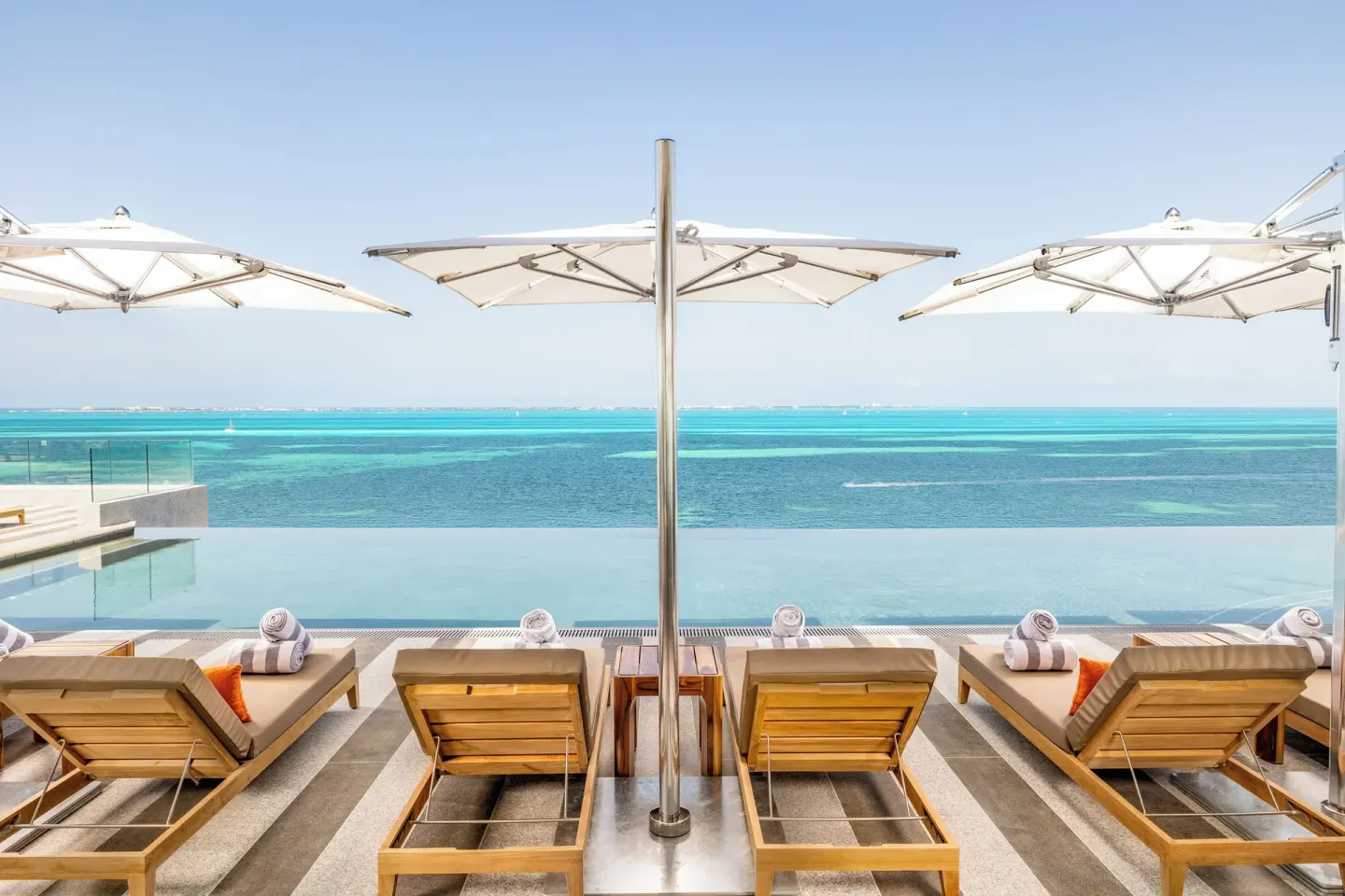 Infinity pool loungers and umbrellas facing the Caribbean at Hotel Mousai Cancun.