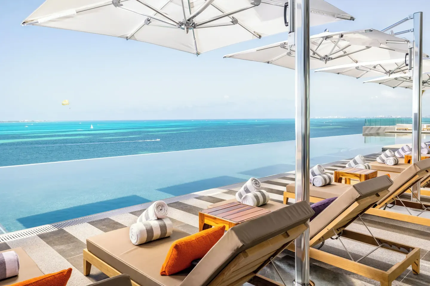 Infinity pool loungers under white umbrellas facing the sea at Hotel Mousai Cancun.