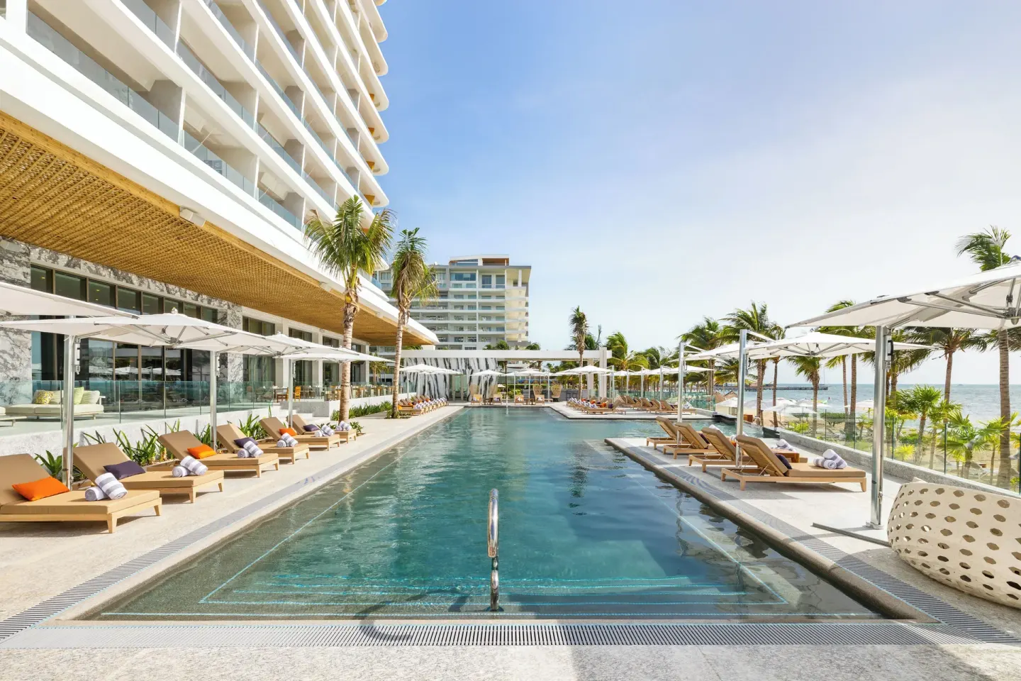 Long resort pool with ocean glimpses and lounge seating at Hotel Mousai Cancun.