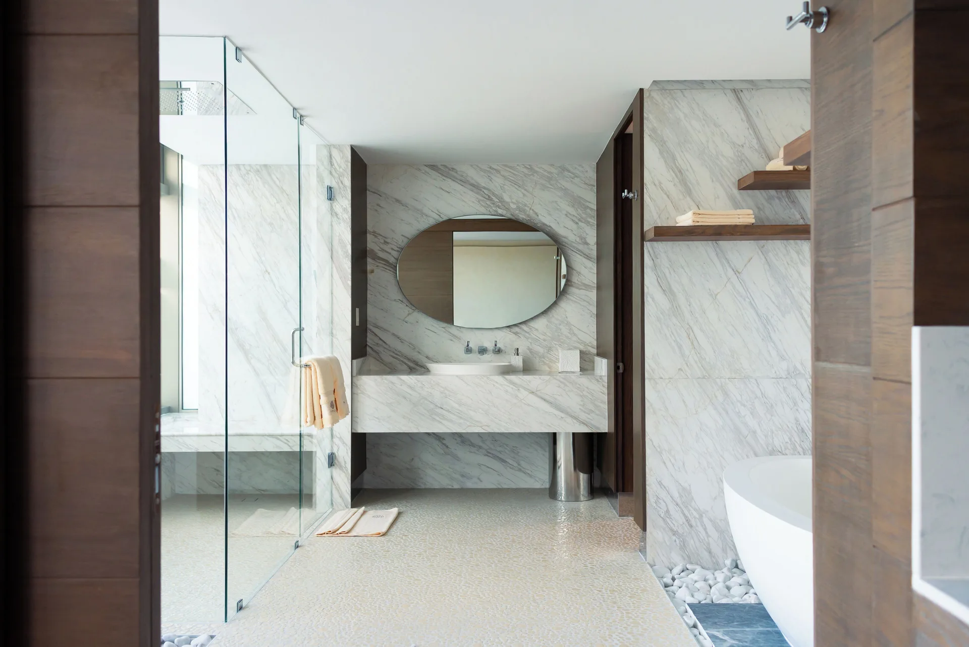 Marble bathroom with glass shower, round mirror, and tub at Hotel Mousai Cancun.