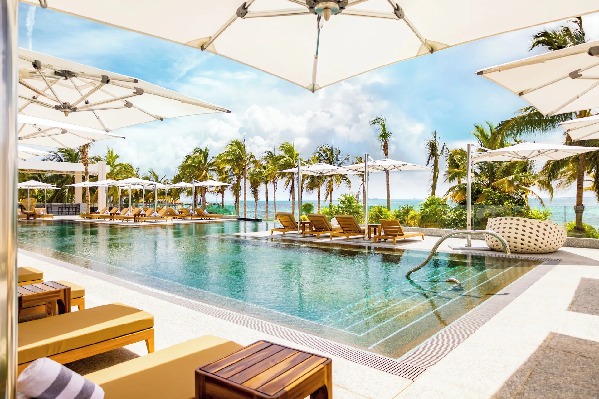 Oceanfront pool with loungers and white umbrellas at Hotel Mousai Cancun.