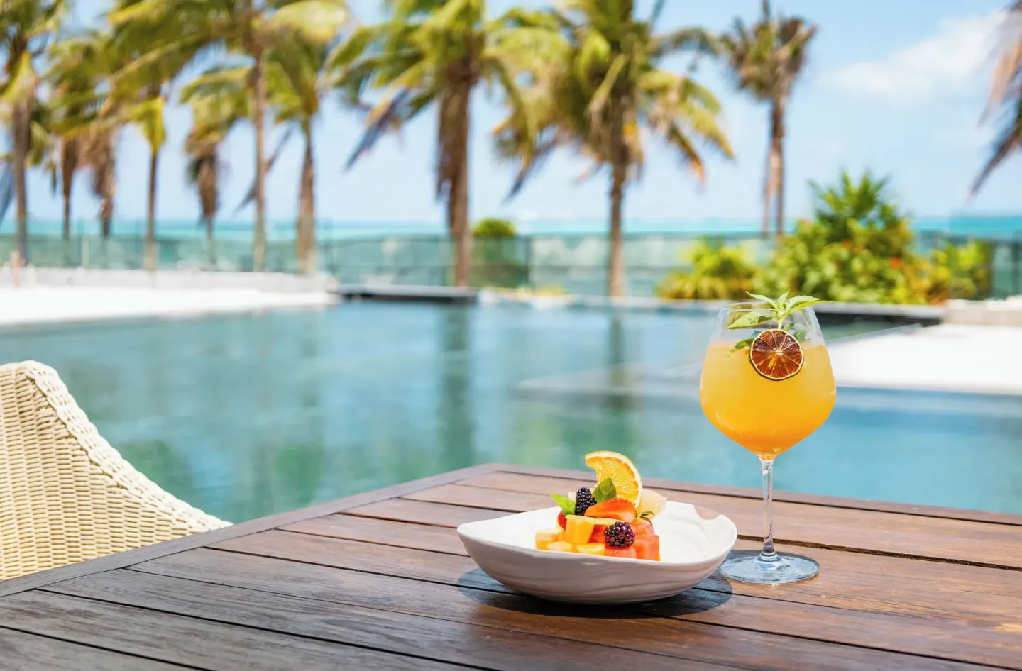 Poolside cocktail and fruit on a wooden table at Hotel Mousai Cancun.