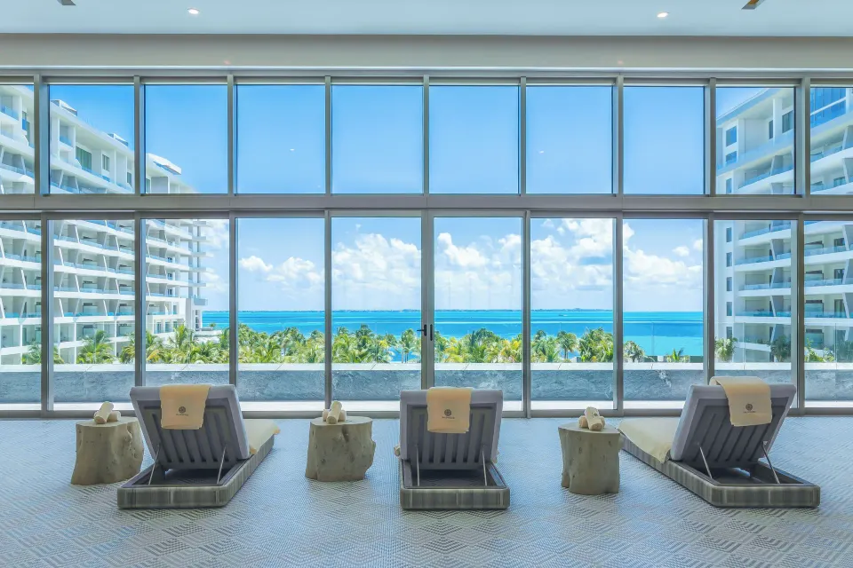 Spa lounge chairs facing large windows and ocean views at Hotel Mousai Cancun.