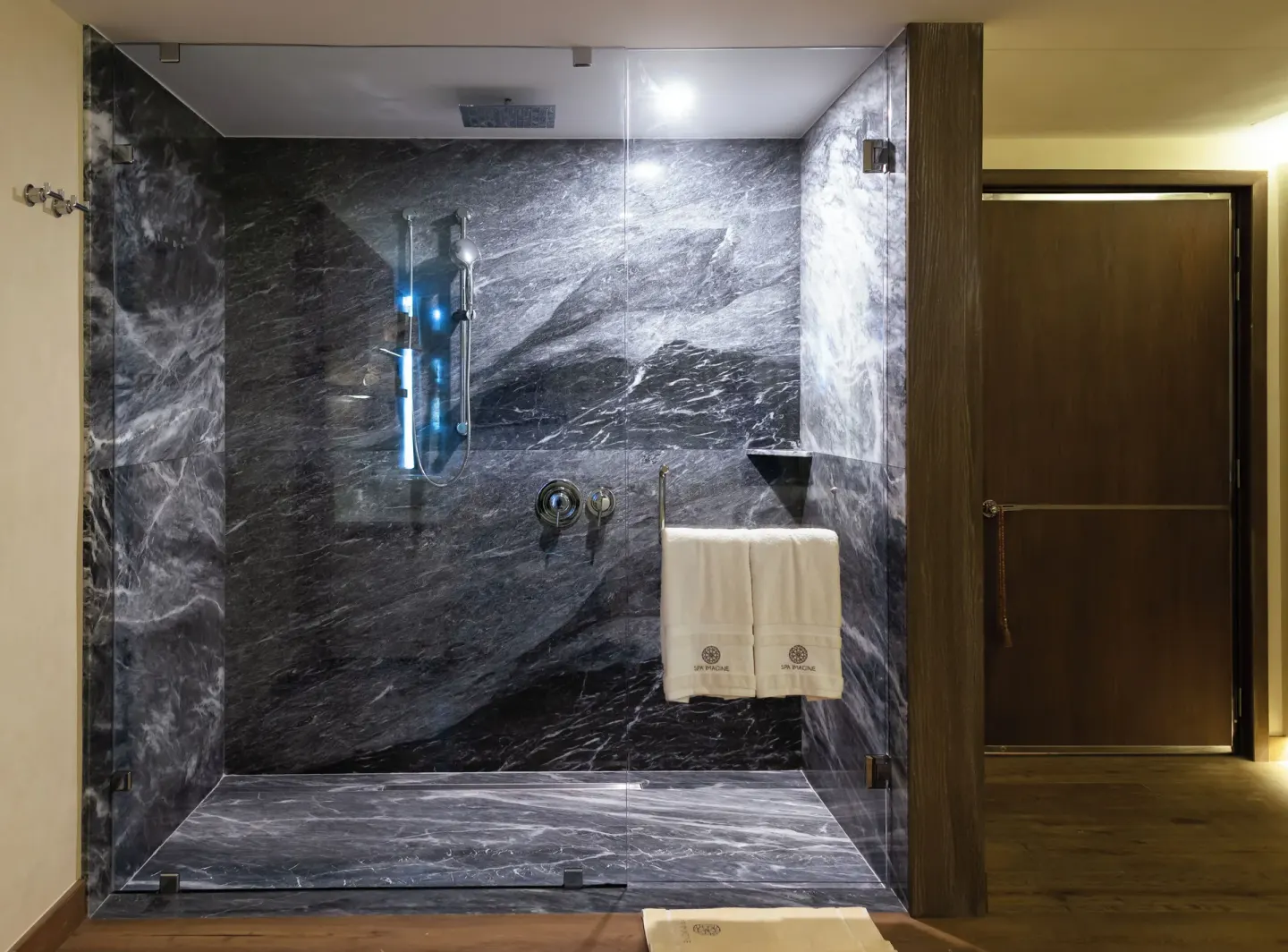 Dark stone spa shower with glass doors and towels at Hotel Mousai Cancun.