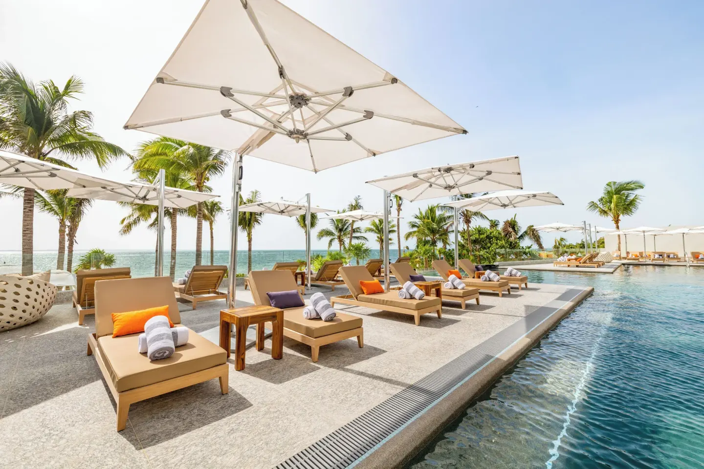 Umbrella-shaded pool deck with loungers and ocean views at Hotel Mousai Cancun.