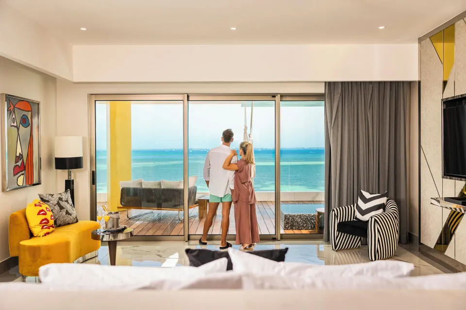 Couple in Corner Suite Ocean Front bedroom looking toward the balcony at Hotel Mousai Cancun.
