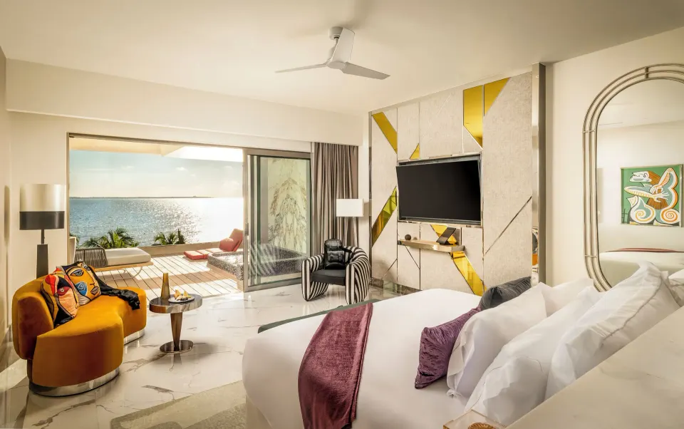 Suite ocean front king bed with seating area and terrace view at Hotel Mousai Cancun.