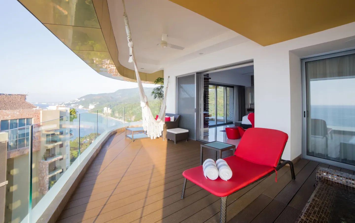 Balcony with red lounger, hammock and coastal view at Hotel Mousai Puerto Vallarta.
