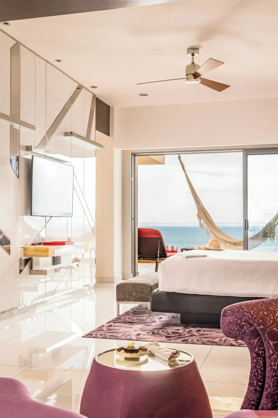 Guest room with king bed, TV wall, hammock balcony and ocean view at Hotel Mousai Puerto Vallarta.