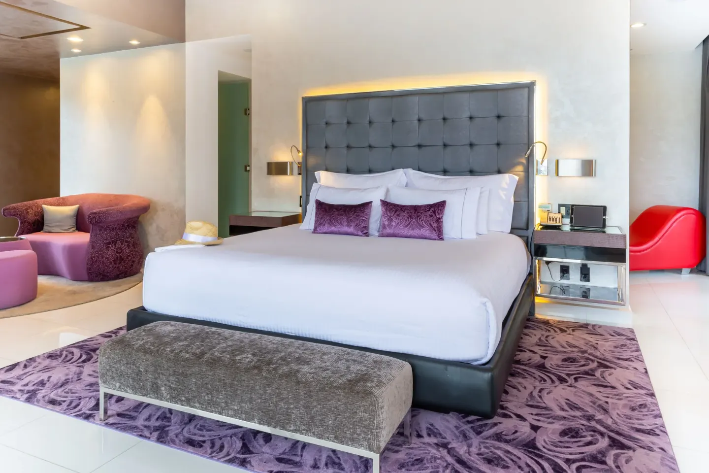 King bed with purple seating and bench in a guest room at Hotel Mousai Puerto Vallarta.