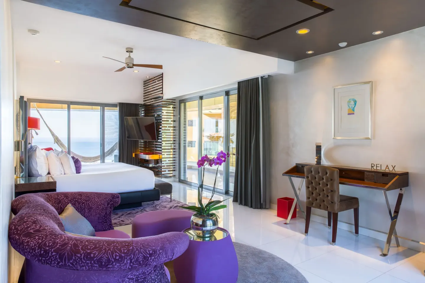 King bed guest room with purple sofa, desk, and ocean-facing balcony at Hotel Mousai Puerto Vallarta.