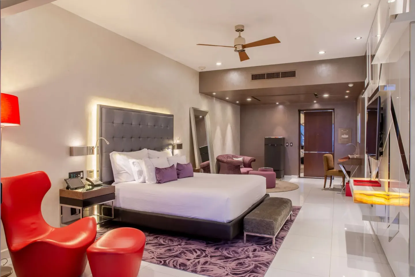King bed guest room with red chair and wall-mounted TV at Hotel Mousai Puerto Vallarta.