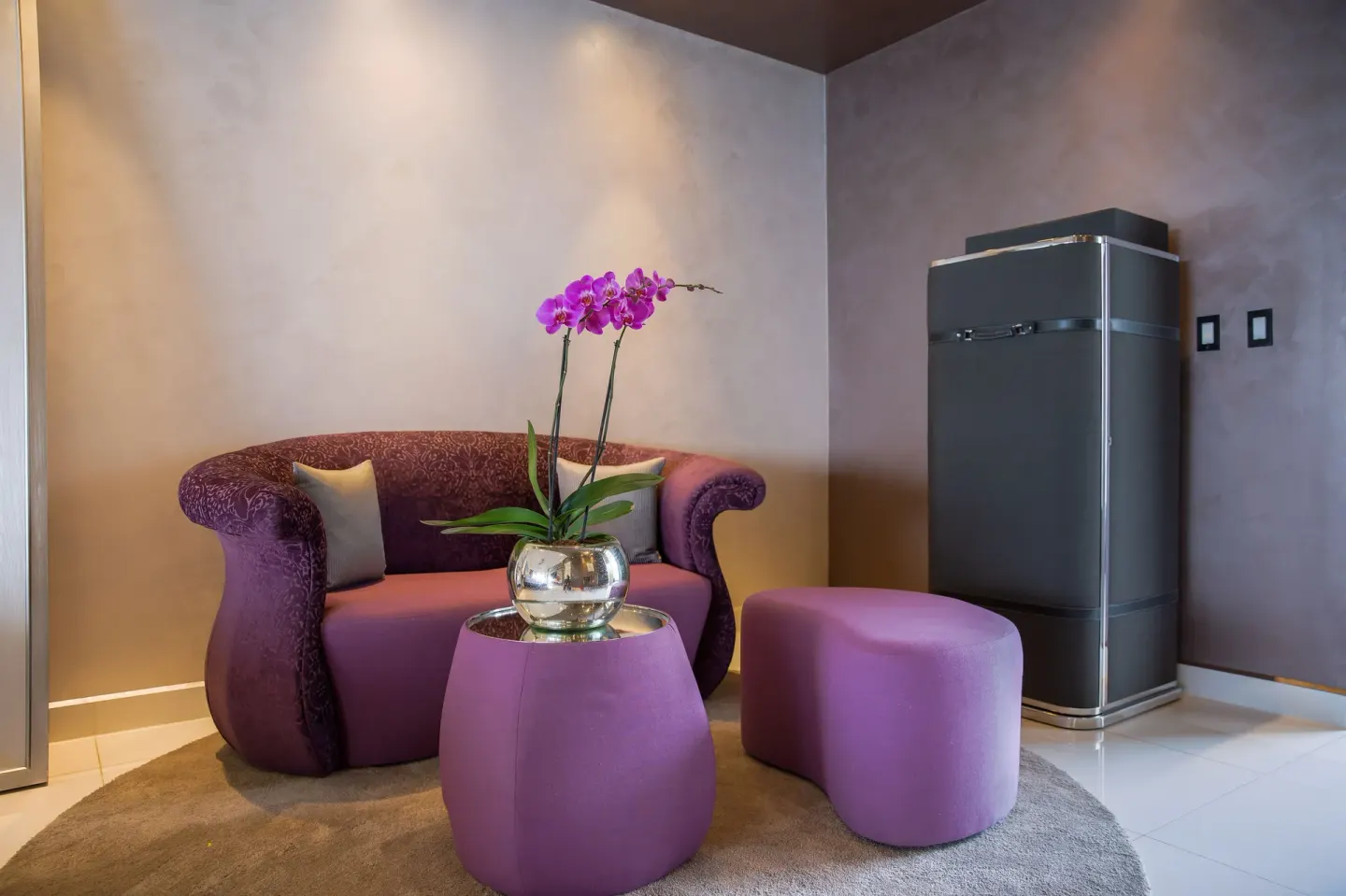 Purple sofa, ottoman, orchid, and tall cabinet in a guest room at Hotel Mousai Puerto Vallarta.