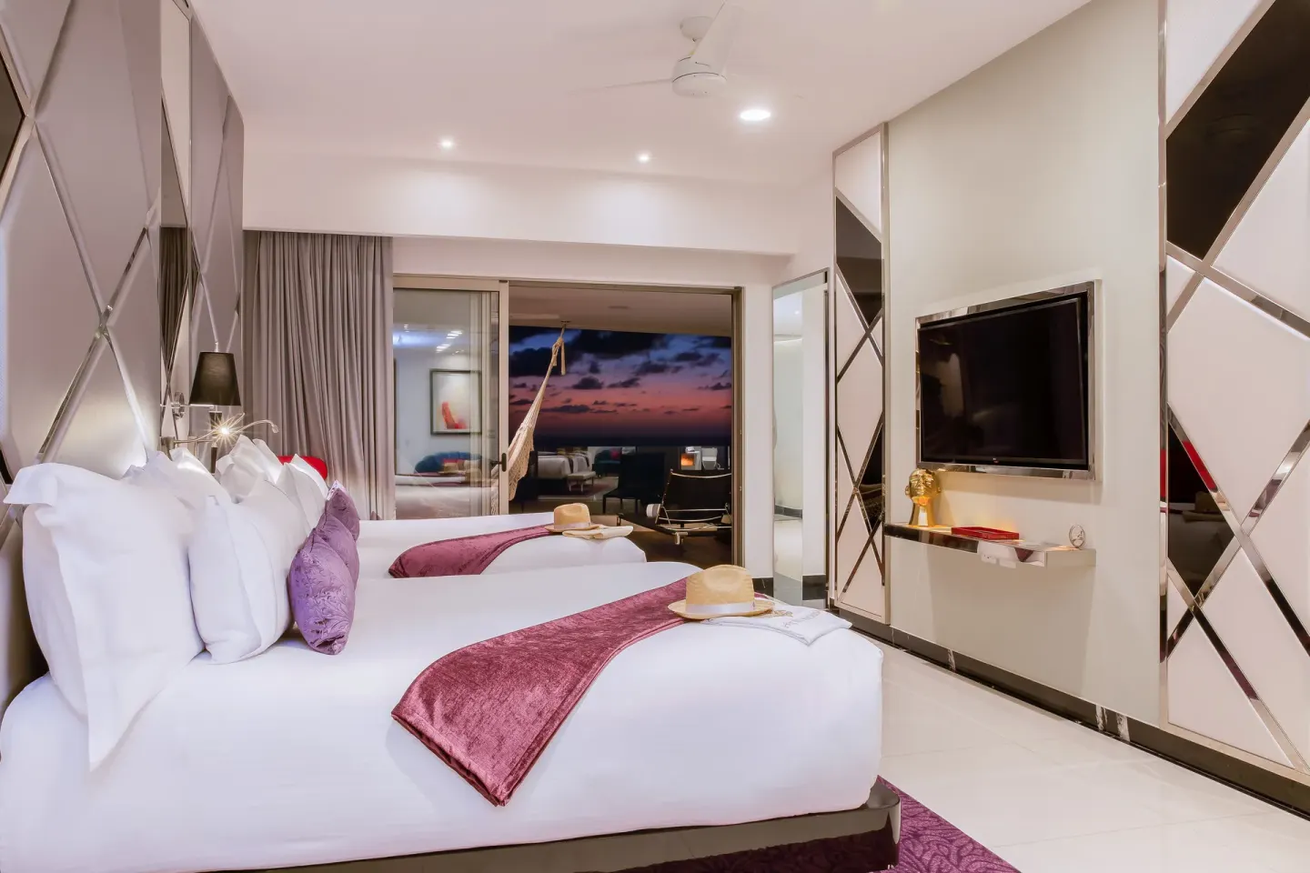 Guest room with two beds, TV, balcony, and sunset view at Hotel Mousai Puerto Vallarta.