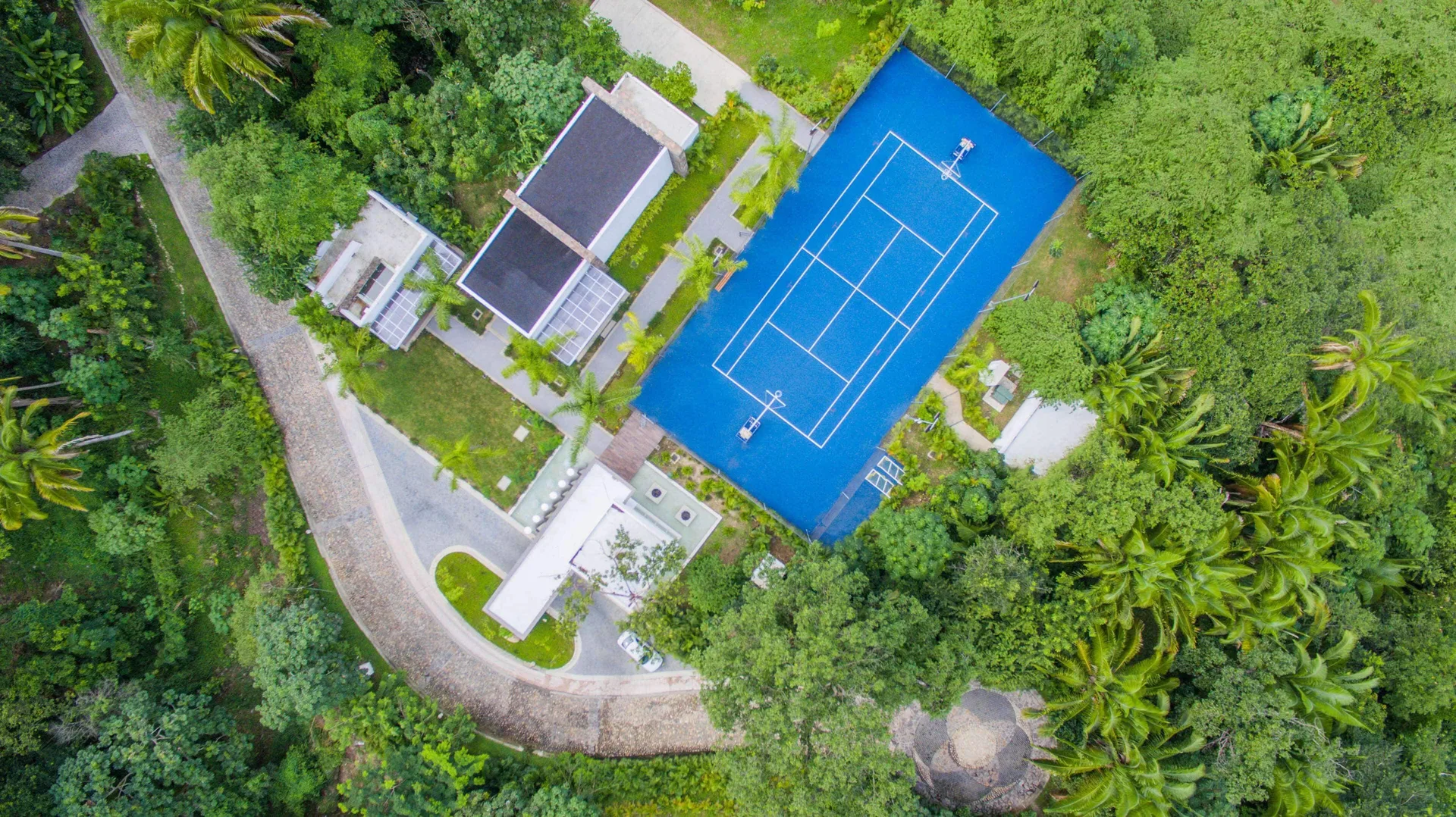 Aerial view of a blue tennis court in the jungle at Hotel Mousai Puerto Vallarta.