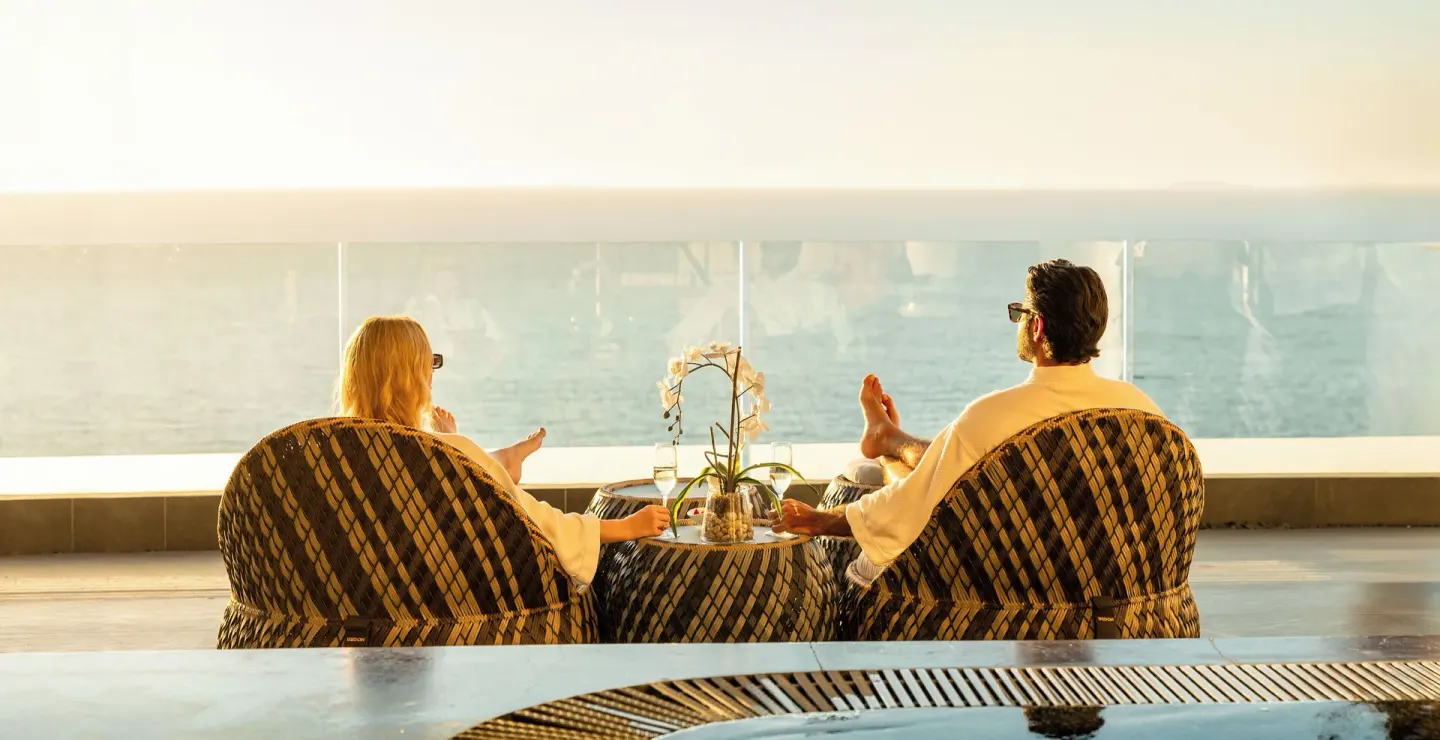 Couple in robes relaxing in lounge chairs facing the ocean at Hotel Mousai Puerto Vallarta.