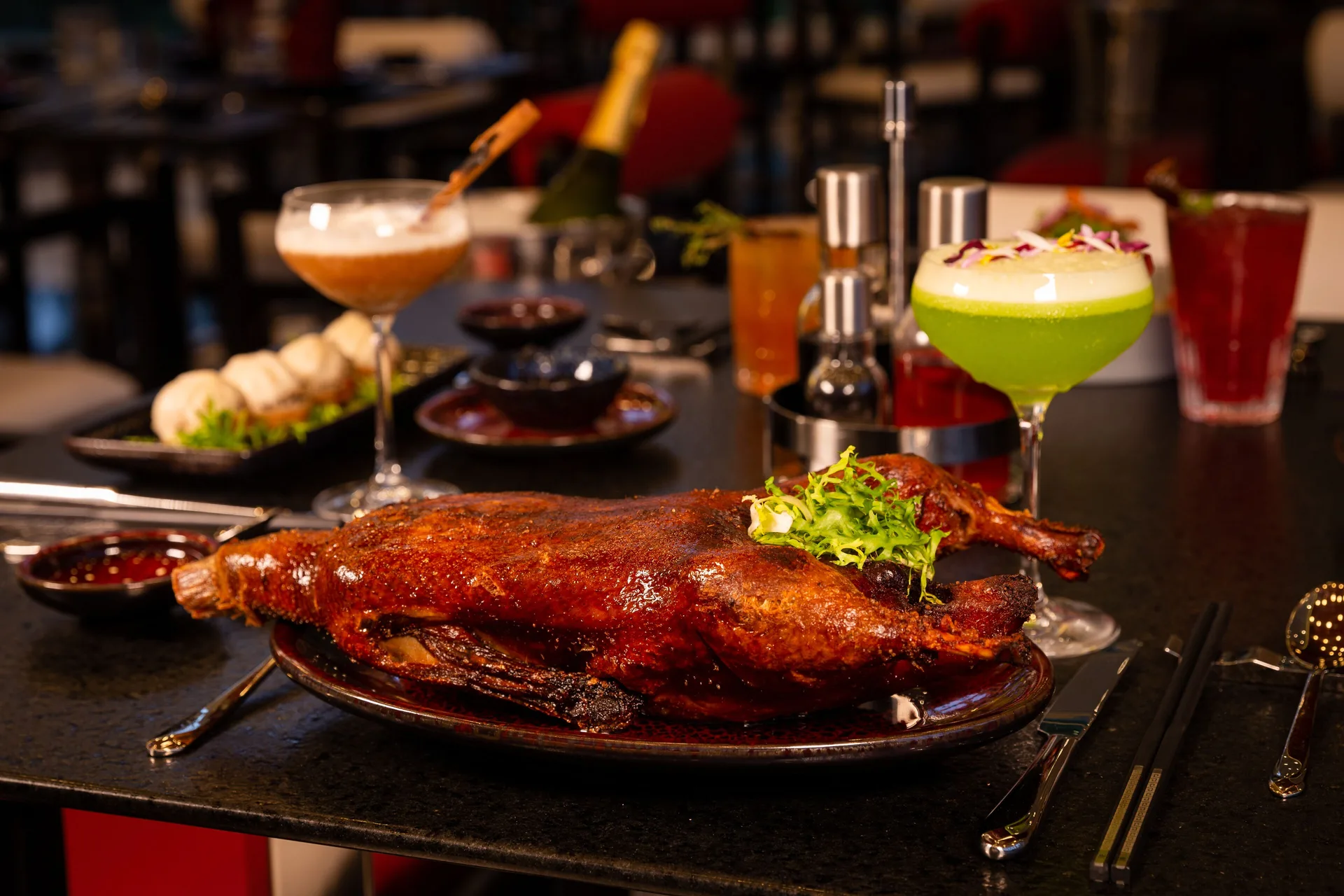 Roasted duck with cocktails on a dark dining table at Hotel Mousai Puerto Vallarta.