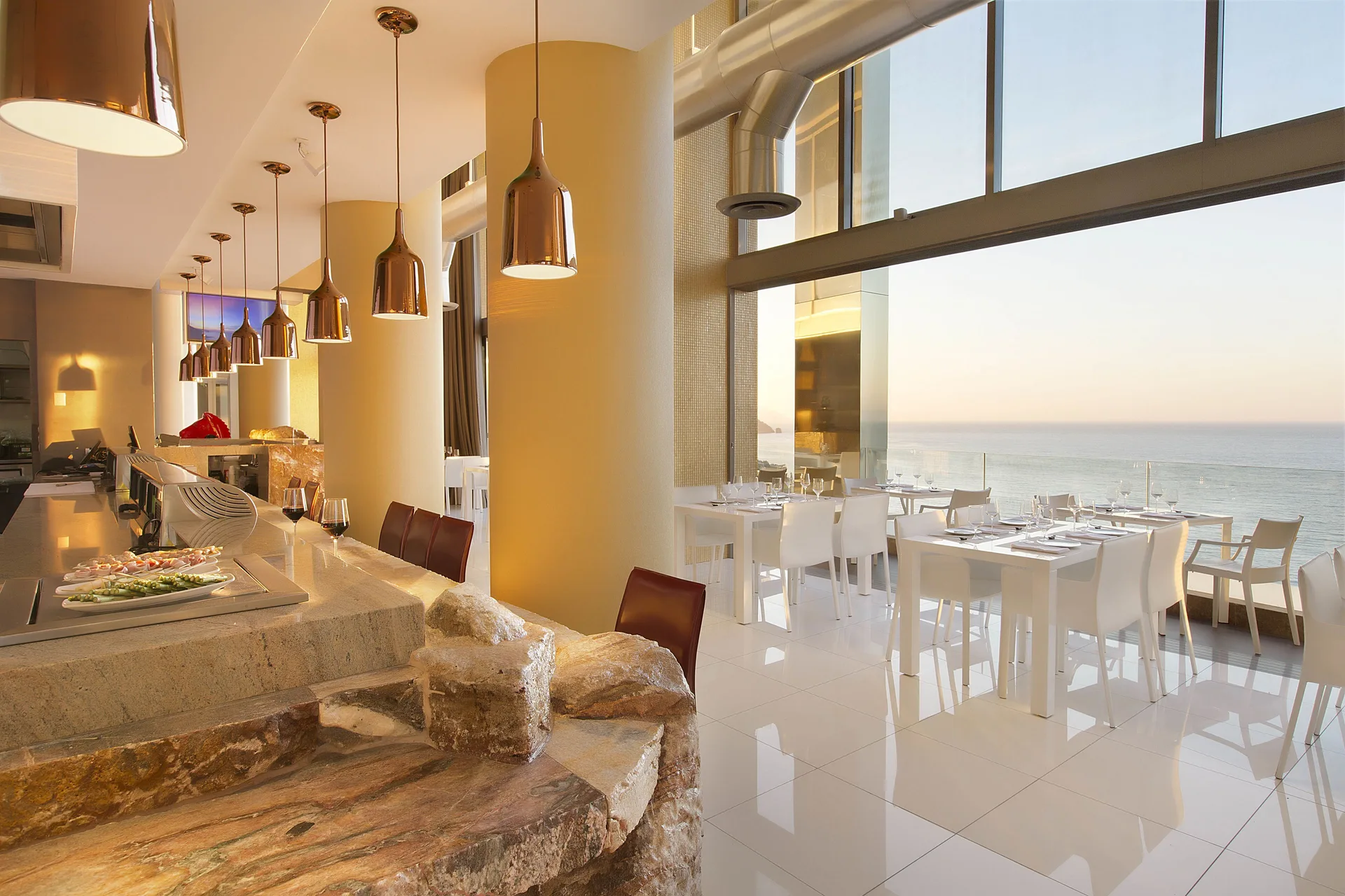 Ocean-view dining room with white tables and pendant lights at Hotel Mousai Puerto Vallarta.