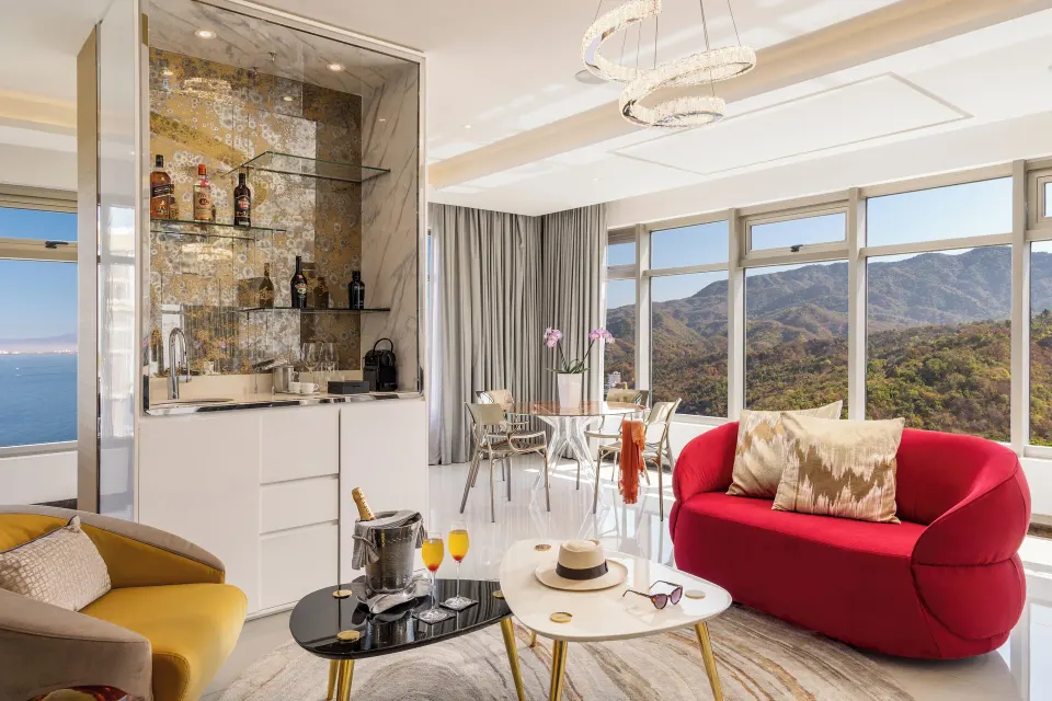 Master Suite living area with red sofa, minibar, dining table, and mountain views at Hotel Mousai Puerto Vallarta.