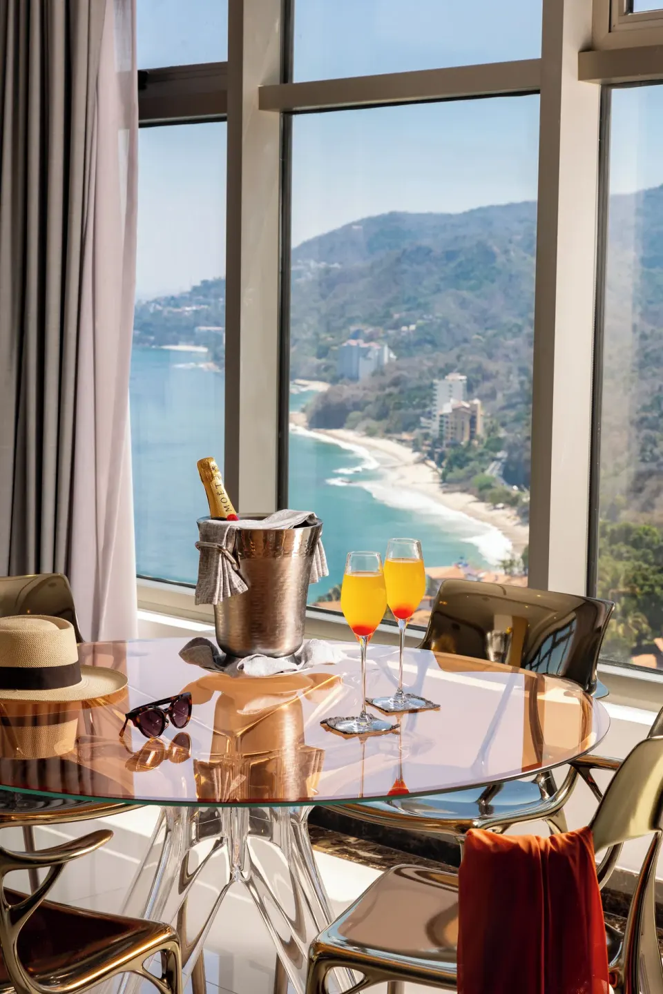 Master Suite table with drinks by tall coastline-view windows at Hotel Mousai Puerto Vallarta.
