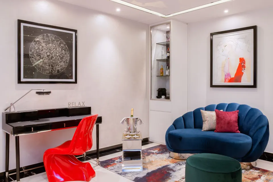 Suite sitting area with blue sofa, red chair, desk, and artwork at Hotel Mousai Puerto Vallarta.