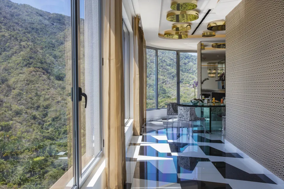 Windowed dining area in The Penthouse at Hotel Mousai Puerto Vallarta overlooking green hills.