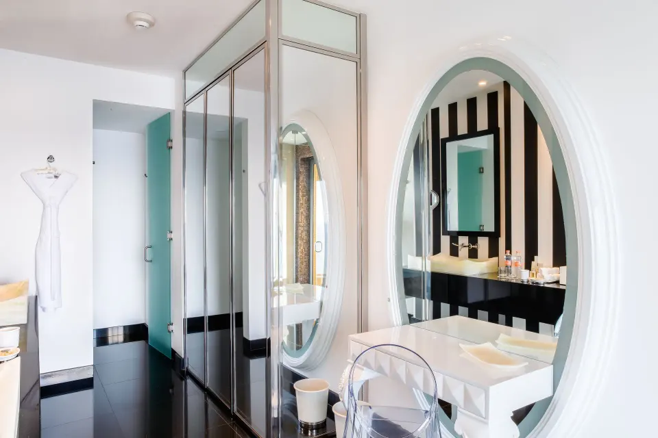 The Penthouse dressing area at Hotel Mousai Puerto Vallarta with oval mirror, glass doors, and vanity chair.