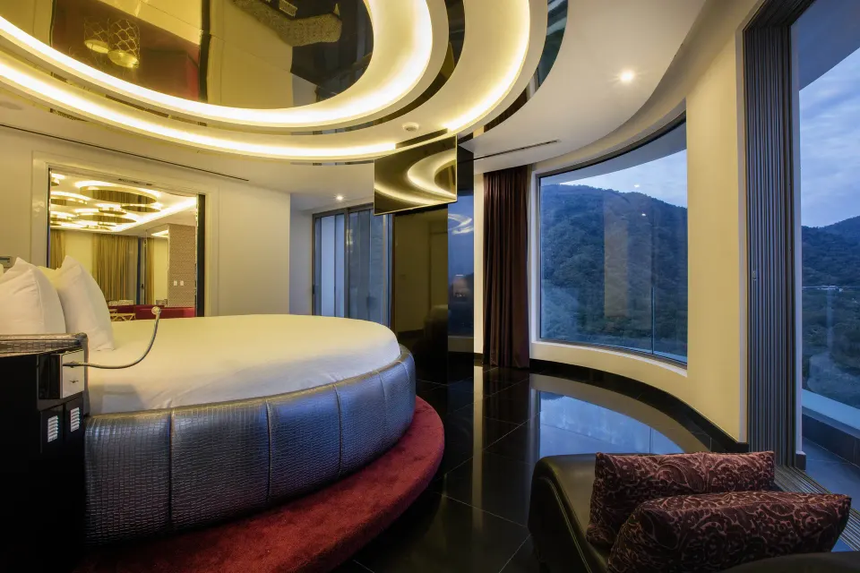 Round king bed in The Penthouse at Hotel Mousai Puerto Vallarta with curved windows and mountain views.