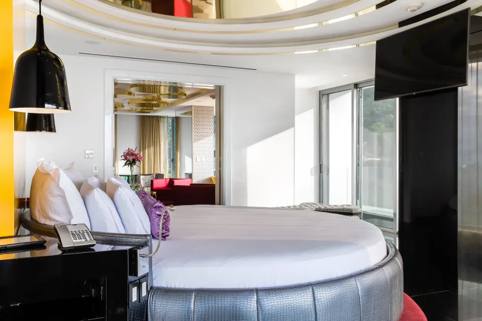 Side view of The Penthouse king bed at Hotel Mousai Puerto Vallarta with TV and balcony doors.