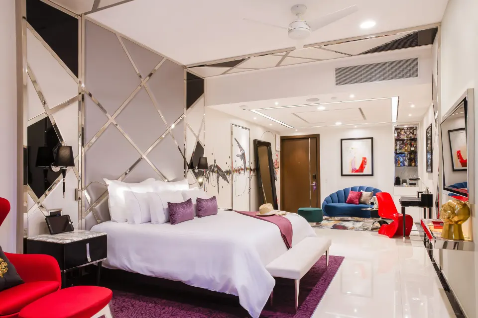 Ultra room with a king bed, red chair, blue sofa, and wall art at Hotel Mousai Puerto Vallarta.