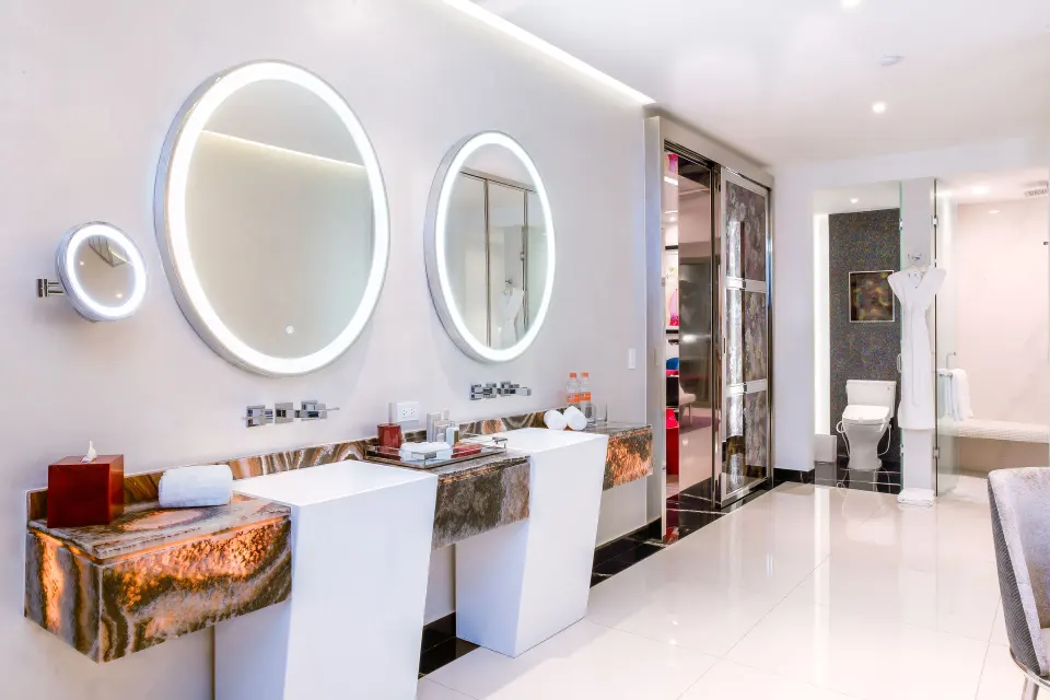 Ultra suite bathroom with double vanities and lit round mirrors at Hotel Mousai Puerto Vallarta.