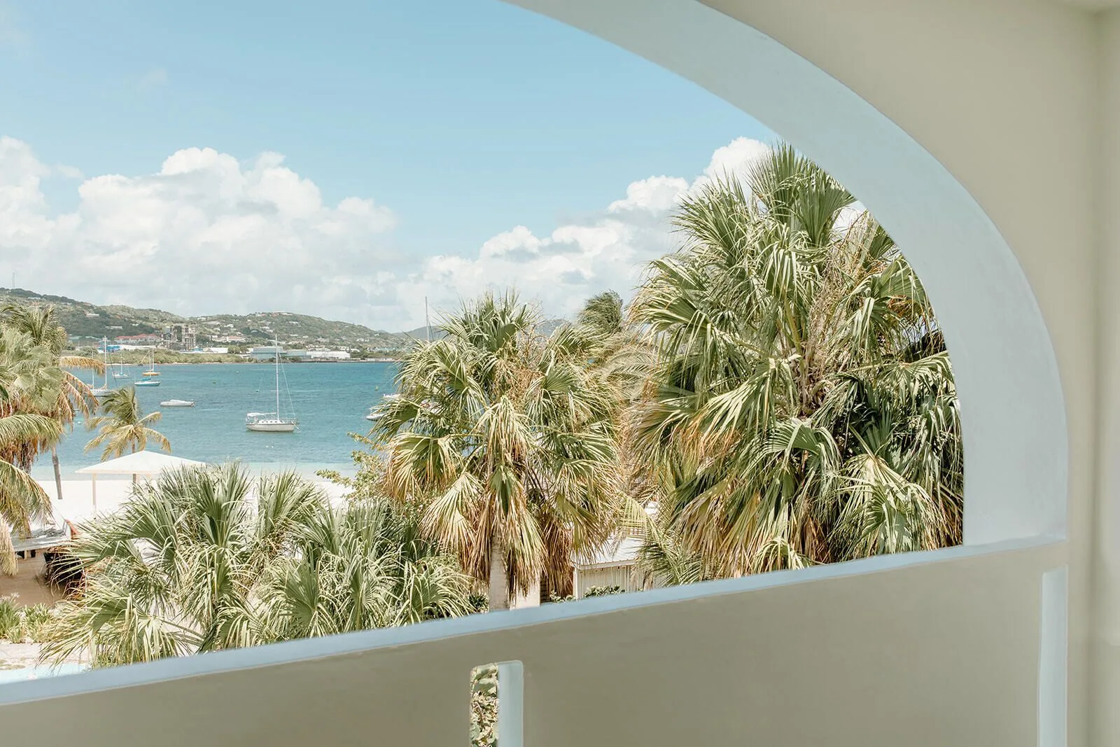 Arched balcony view of palm trees, blue water, sailboats, and hills at Hotel on the Cay.