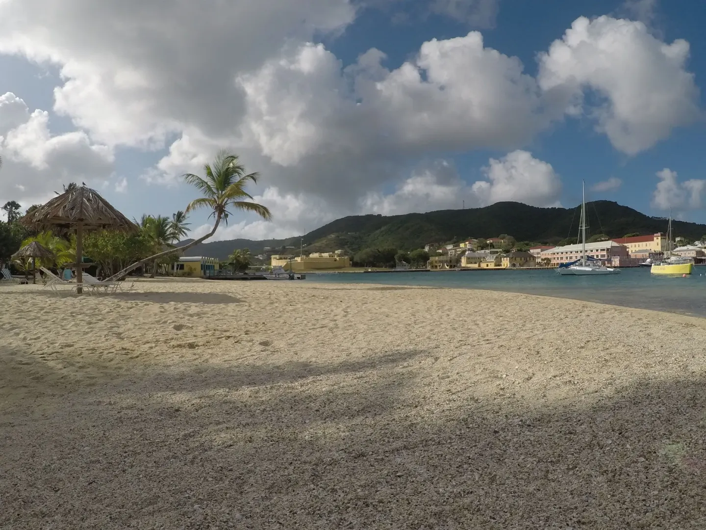 Beach with thatched shade, harbor boats and hillside town views at Hotel on the Cay.
